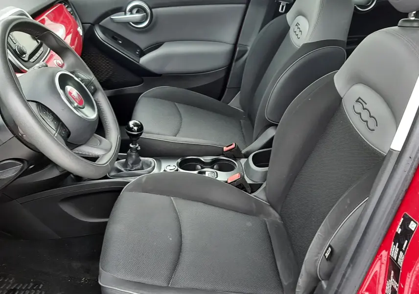 Vue intérieure côté conducteur d'une FIAT 500X rouge, sièges gris foncé avec logo 500 embossé sur les appuie-têtes.