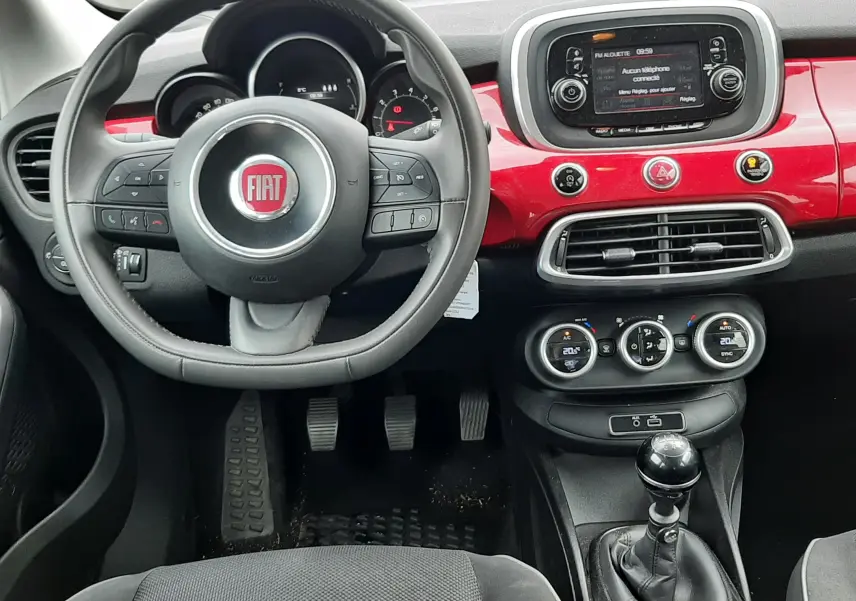 Vue rapprochée du volant noir avec logo rouge FIAT du tableau de bord d'une 500X rouge de 2016.