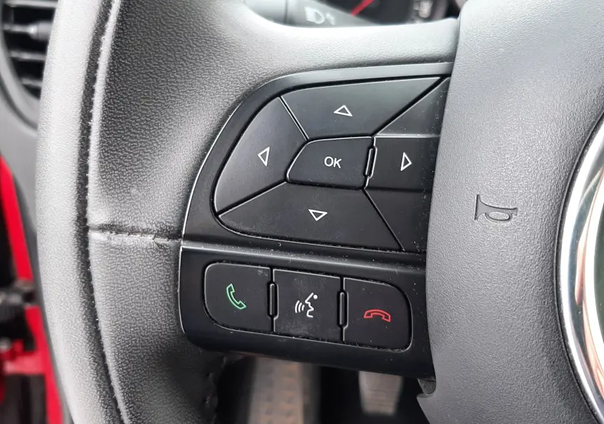 Gros plan sur les commandes de régulateur de vitesse au volant noir d'une Fiat 500X rouge de 2016.