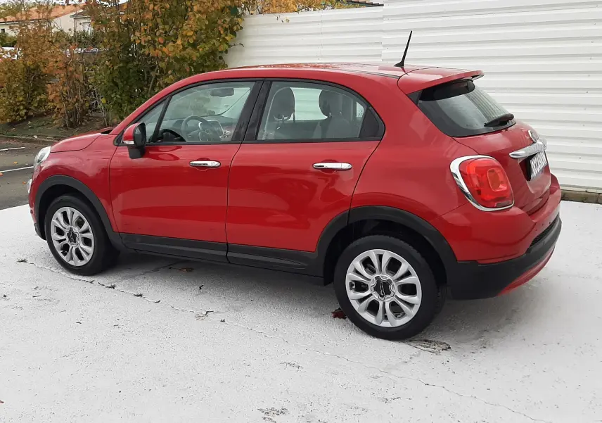 Vue 3/4 arrière droite d'une FIAT 500X rouge 5 portes avec jantes alliage et plaque "OCCASION" visible.