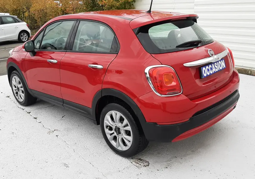 Vue 3/4 arrière droite d'une FIAT 500X rouge avec plaque "OCCASION" sur parking extérieur.