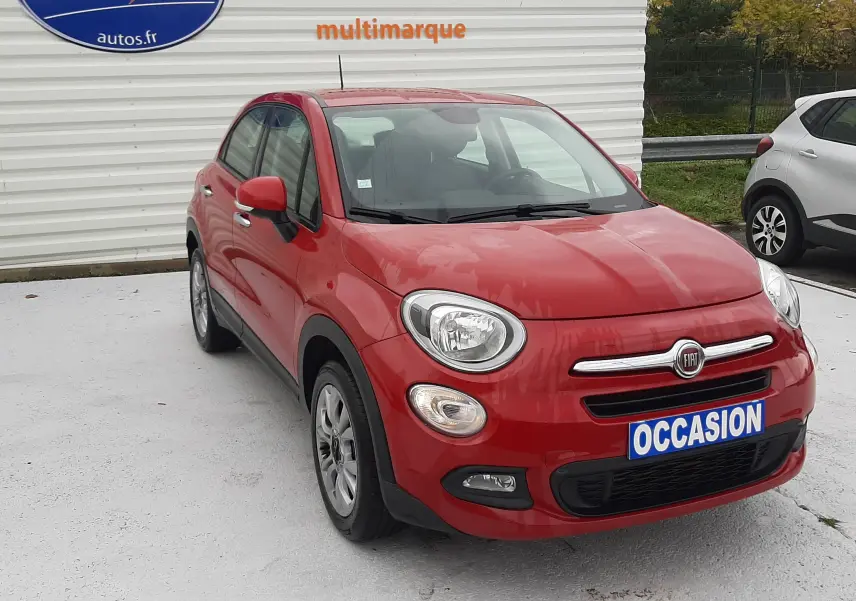 Vue de profil côté gauche d'une Fiat 500X rouge 5 portes garée devant un mur blanc avec logo bleu.