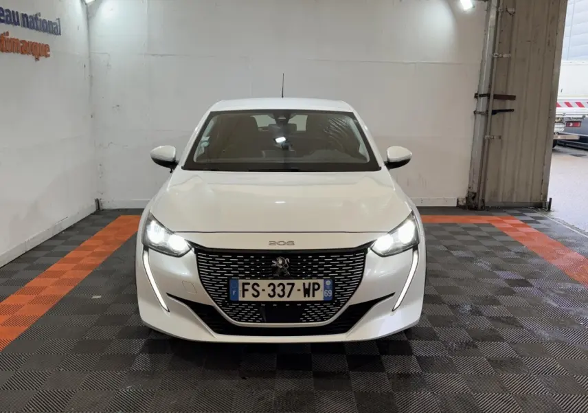 Peugeot 208 électrique blanche vue de face, avec phares LED allumés dans un garage.