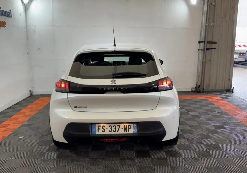 Vue arrière d'une Peugeot 208 électrique Active Business blanche, avec feux arrière allumés et plaque d'immatriculation visible.
