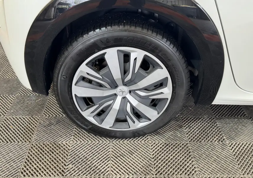 Gros plan sur la roue avant droite d'une Peugeot 208 électrique blanche, avec jante en alliage au design moderne.