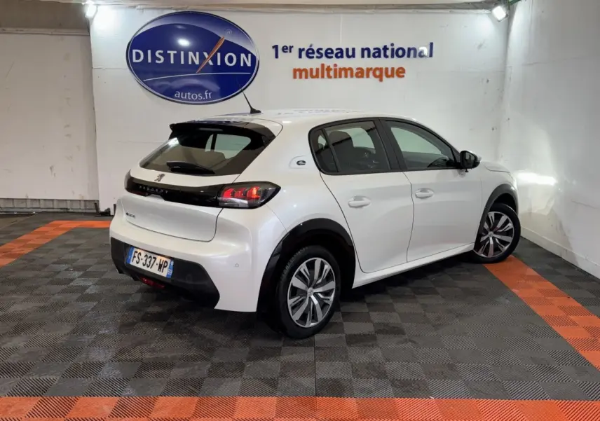 Vue 3/4 arrière droite d'une Peugeot 208 électrique blanche avec feux LED et jantes spécifiques, en intérieur showroom.