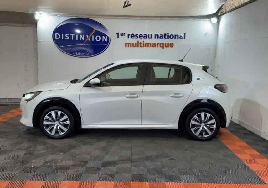 Peugeot 208 Electrique Active Business vue de profil côté gauche, couleur blanche, en intérieur sur sol damier noir et orange.