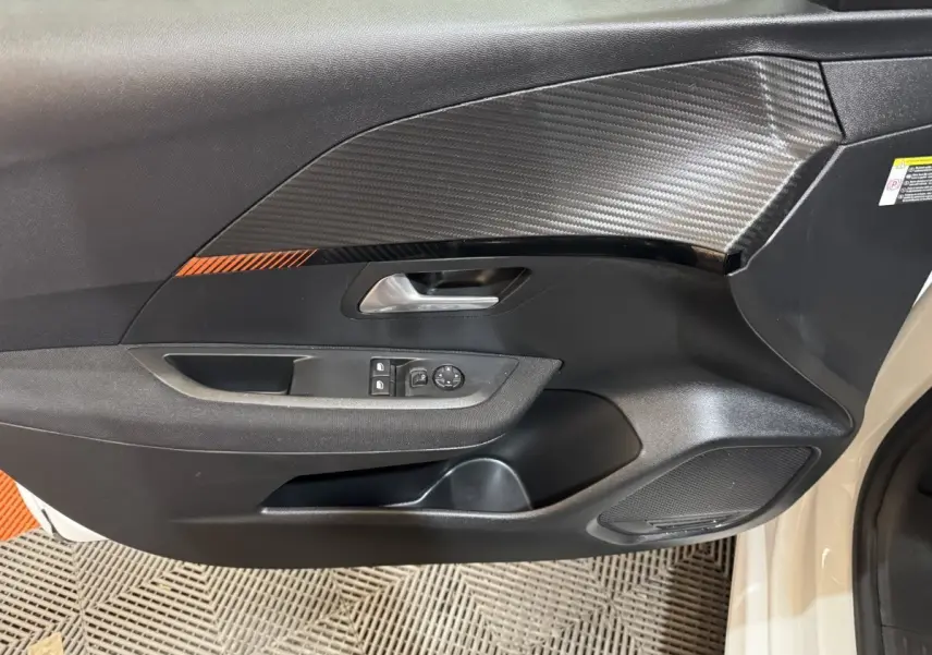 Vue rapprochée de la porte avant gauche noire avec insert effet carbone et commandes des vitres de la Peugeot 208 électrique.