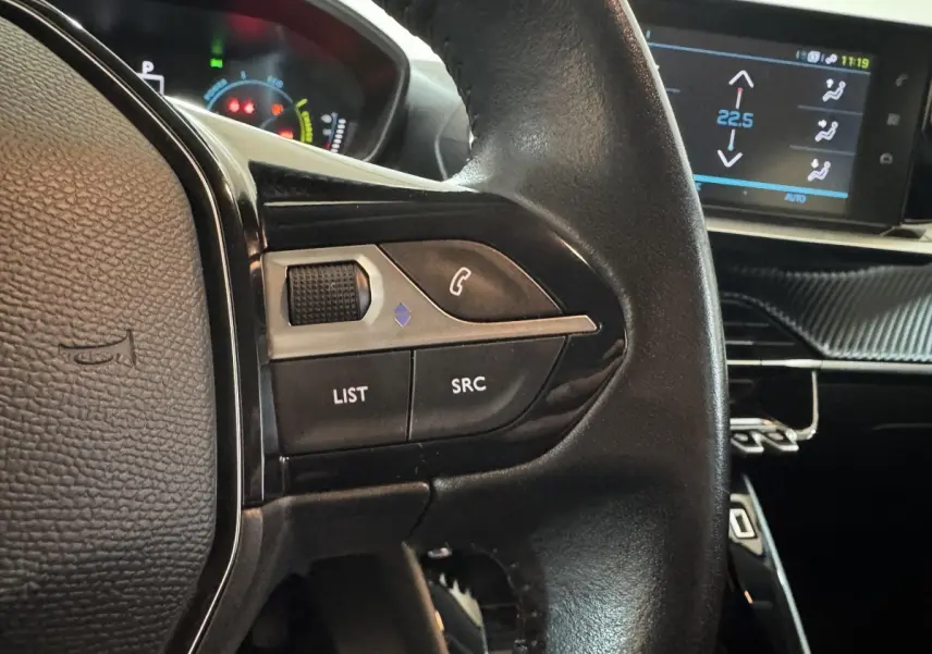 Gros plan sur les commandes gauche du volant cuir noir de la Peugeot 208 électrique Active Business avec écran tactile en arrière-plan.