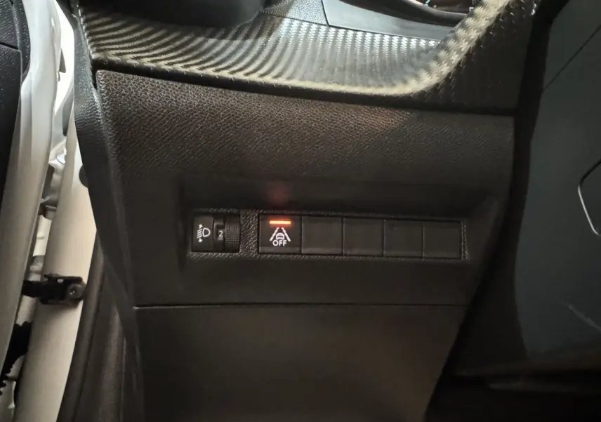Gros plan sur les commandes noires du tableau de bord côté gauche d’une Peugeot 208 électrique, bouton d’aide à la conduite désactivé.