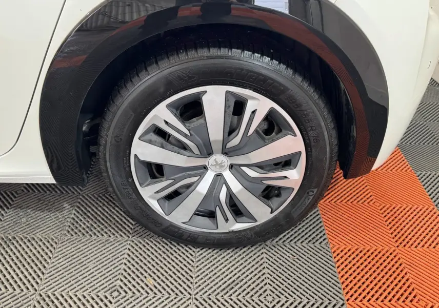 Gros plan sur la roue arrière droite d'une Peugeot 208 électrique blanche avec jante aluminium et passage de roue noir.