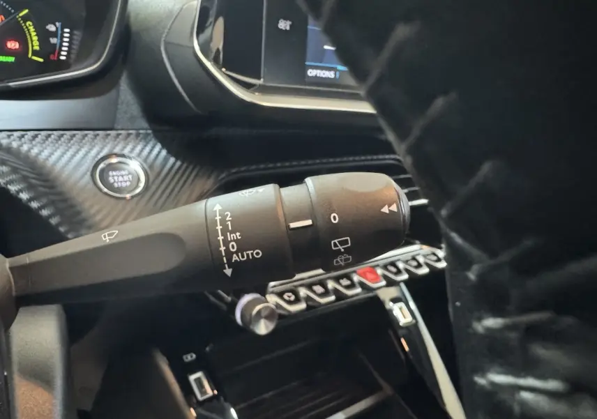 Gros plan sur la commande d’essuie-glace et bouton démarrage dans l’habitacle noir d’une Peugeot 208 électrique.