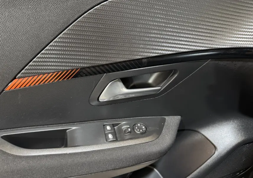 Détail de la porte intérieure côté conducteur de la Peugeot 208 électrique Active Business avec insert carbone et bande orange.