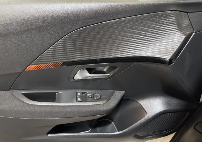 Vue rapprochée de la porte intérieure côté gauche de la Peugeot 208 électrique avec insert carbone et bande orange.