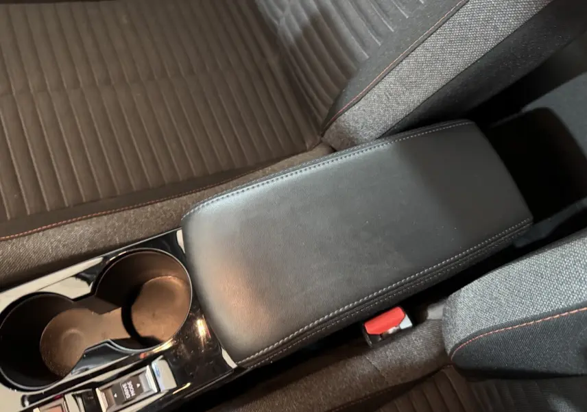 Vue rapprochée de l'accoudoir central noir et des sièges gris avec surpiqûres rouges dans une Peugeot 208 électrique.