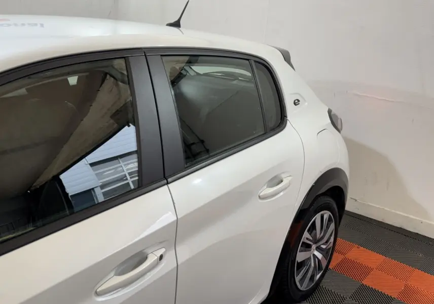 Vue 3/4 arrière droite d’une Peugeot 208 électrique blanche avec logo « e » sur l’aile arrière et jantes spécifiques.