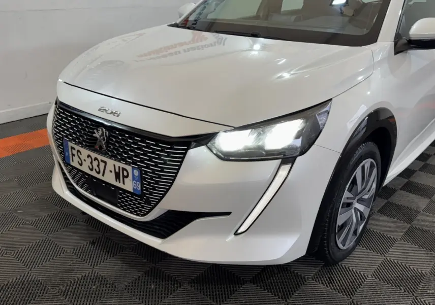 Vue 3/4 avant droit d'une Peugeot 208 électrique blanche avec phares LED allumés et calandre noire distinctive.