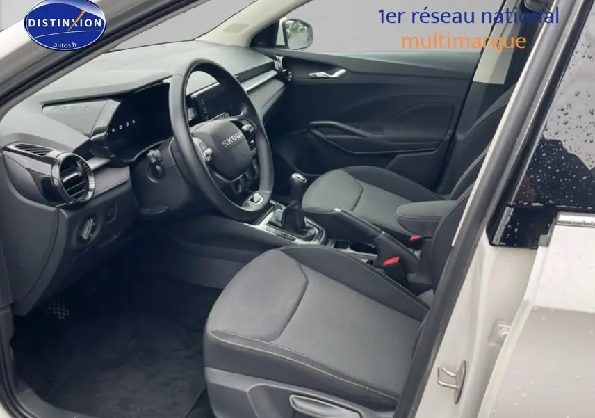 Vue intérieure côté conducteur d'une Skoda Fabia blanche 2025, montrant le tableau de bord et les sièges noirs.