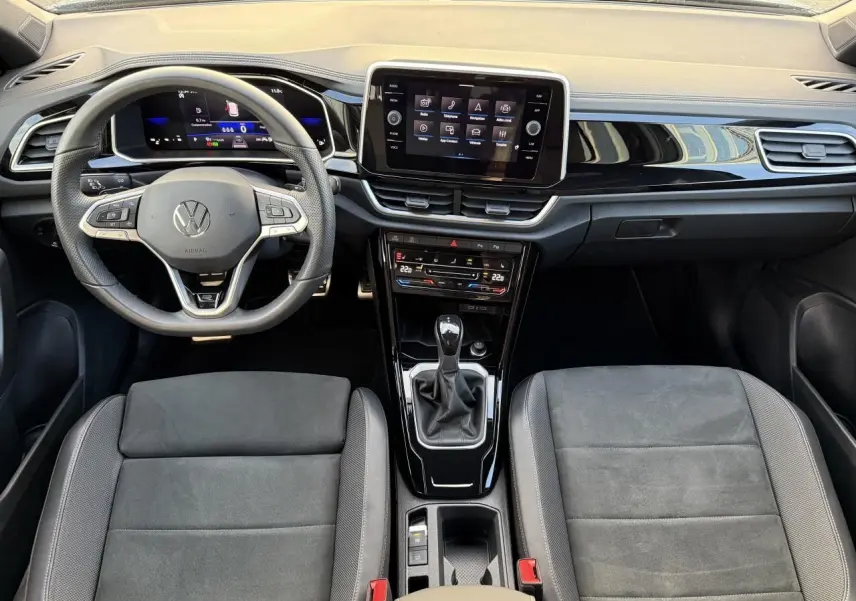 Vue intérieure avant du Volkswagen T-Roc 2025 avec tableau de bord noir, volant multifonction et console centrale avec boîte manuelle.