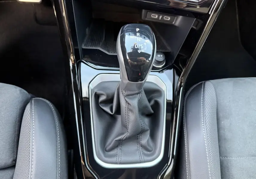Gros plan sur le levier de vitesse manuel noir entouré de cuir, entre les sièges avant gris du Volkswagen T-Roc 2025.