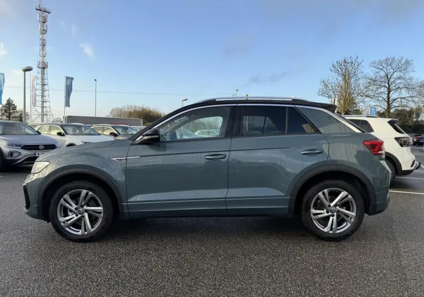 Vue de profil côté gauche d'un Volkswagen T-Roc bleu avec jantes alliage et barres de toit chromées.