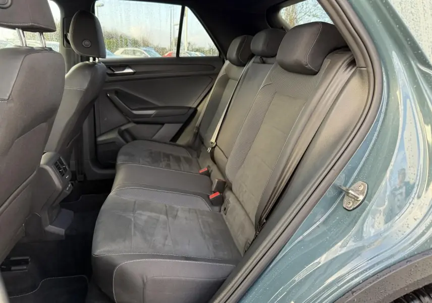 Vue côté droit de l'habitacle arrière du Volkswagen T-Roc 2025 bleu, sièges tissu et alcantara noirs avec ceintures de sécurité.