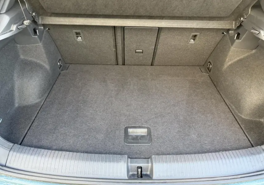 Coffre ouvert du Volkswagen T-Roc bleu, vue plongeante sur l'espace de chargement vide et tapis gris.