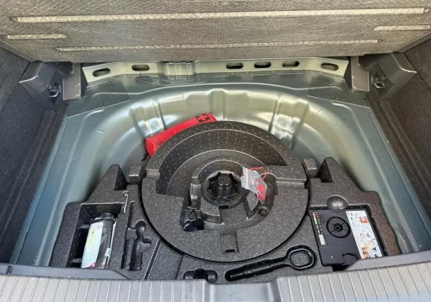 Coffre ouvert du Volkswagen T-Roc 2025 montrant le rangement sous plancher avec kit de dépannage et outils.