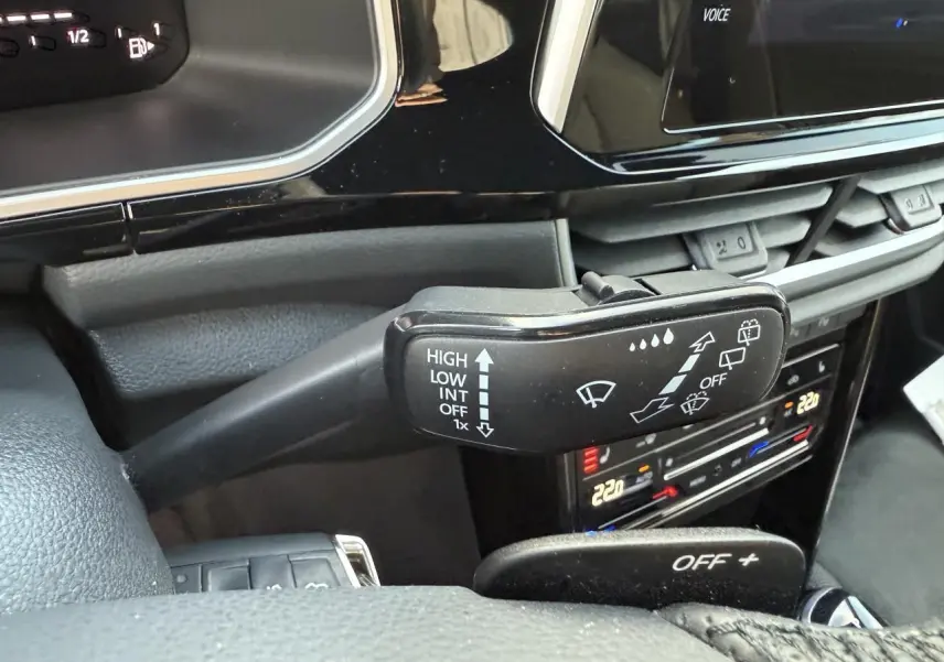 Gros plan sur la commande d’essuie-glace noire dans l’habitacle du Volkswagen T-Roc bleu, avec tableau de bord et climatisation tactile visibles.