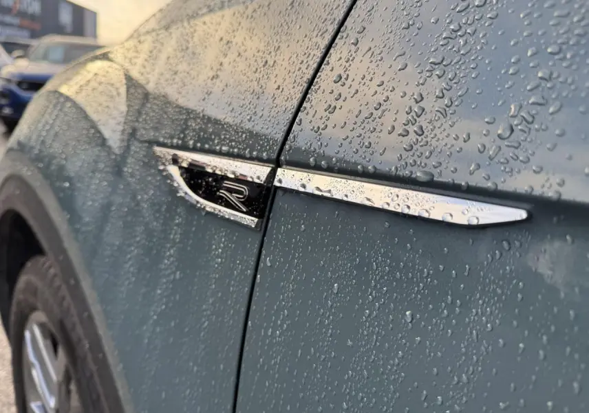 Détail de l'aile avant gauche bleu métallisé du Volkswagen T-Roc avec logo R sous la pluie.
