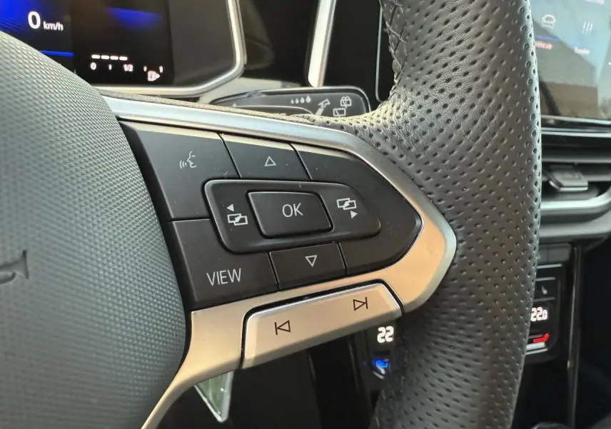 Gros plan sur le volant perforé noir du Volkswagen T-Roc 2025 avec commandes multifonctions et écran digital en arrière-plan.
