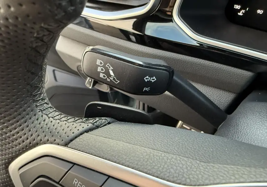 Gros plan sur la manette de clignotants noire à gauche du volant perforé du Volkswagen T-Roc bleu 2025.