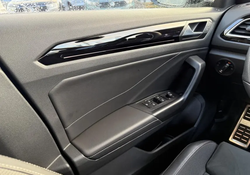 Vue intérieure côté gauche de la porte avant d’un Volkswagen T-Roc bleu, avec garniture noire et commandes électriques.