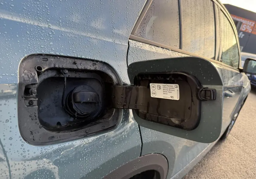 Vue rapprochée de la trappe à carburant ouverte côté gauche d’un Volkswagen T-Roc bleu avec gouttes d’eau.