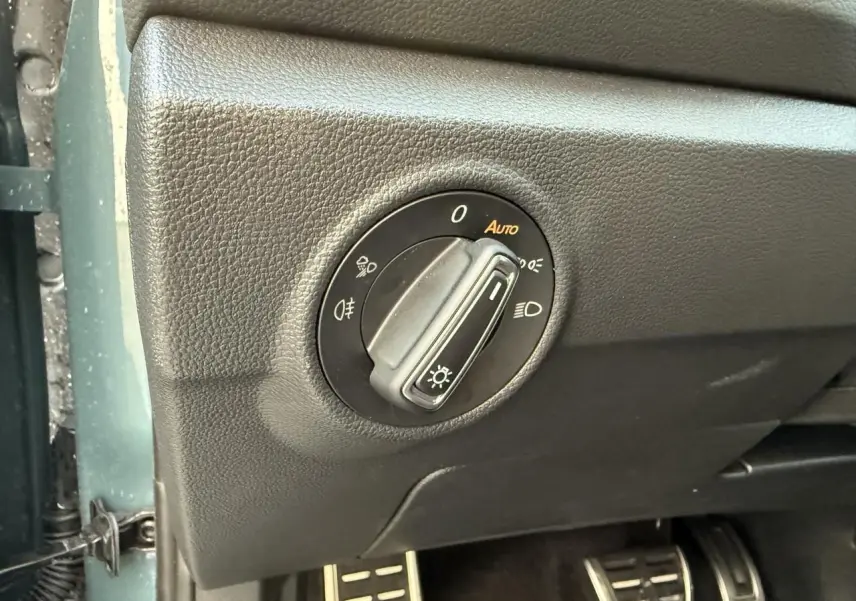 Gros plan sur la commande des feux et pédalier en acier inoxydable dans l'habitacle noir du Volkswagen T-Roc bleu.