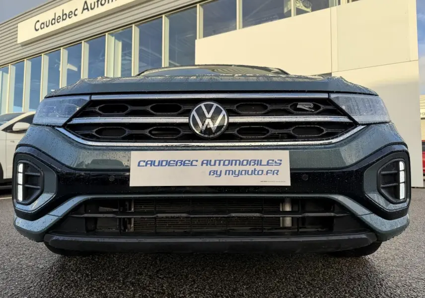 Vue frontale rapprochée du Volkswagen T-Roc bleu avec calandre hexagonale et logo R visible sur la grille.