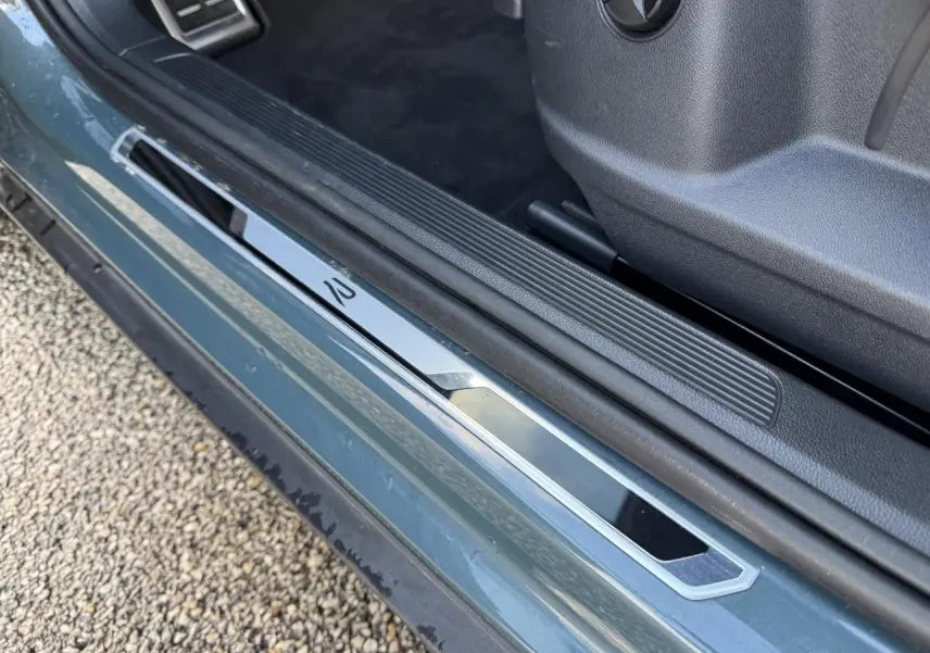 Gros plan sur le seuil de porte côté conducteur bleu du Volkswagen T-Roc avec logo R-Line argenté.