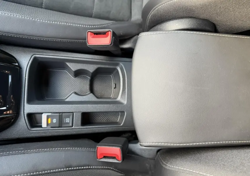 Vue plongeante sur la console centrale noire du Volkswagen T-Roc 2025, avec accoudoir et boutons de frein de stationnement.