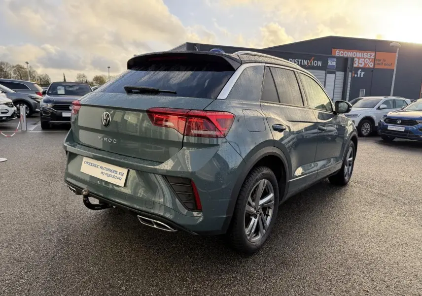 Vue 3/4 arrière droite d'un Volkswagen T-Roc bleu avec attelage amovible et jantes alliage gris galvanisé.