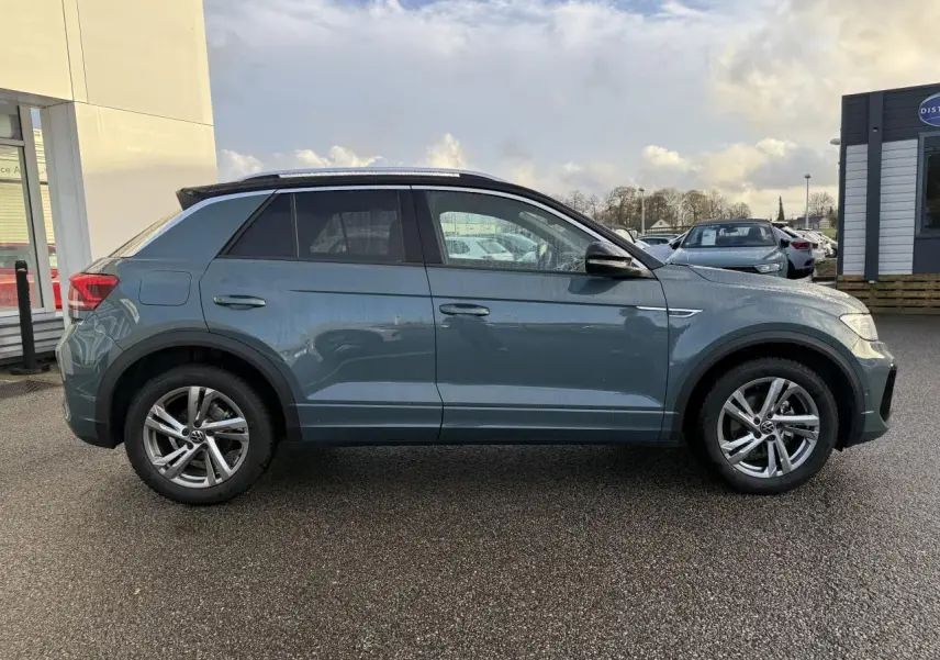 Profil côté gauche d'un Volkswagen T-Roc bleu 2025 avec jantes alliage 17 pouces et toit noir.