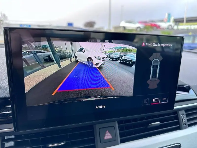 Écran de caméra de recul montrant une voiture blanche en stationnement avec lignes de guidage orange et bleu.