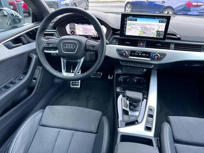 Intérieur noir de l'Audi A5 Cabriolet 35 TFSI 2023 vu de face, avec volant multifonction et écran tactile GPS.