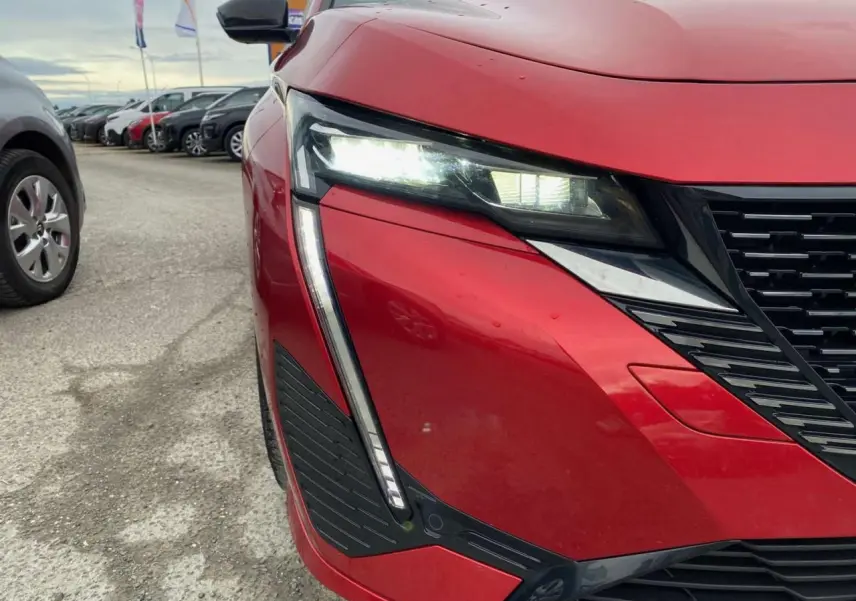Gros plan sur l'avant droit de la Peugeot 308 rouge Elixir avec ses phares LED et la calandre noire distinctive.