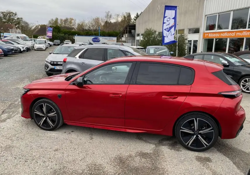 Profil latéral droit de la Peugeot 308 GT 2022 rouge Elixir avec jantes noires et vitres teintées sur parking extérieur.