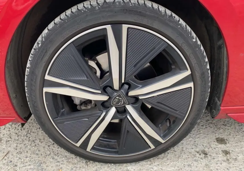 Gros plan sur la roue avant gauche d'une Peugeot 308 rouge Elixir avec jante alliage au design moderne.