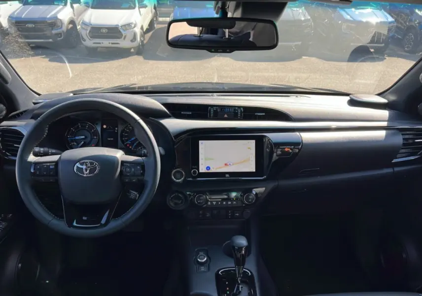 Vue intérieure du Toyota Hilux 2025 Invincible 4x4, tableau de bord noir avec écran tactile et volant multifonctions.