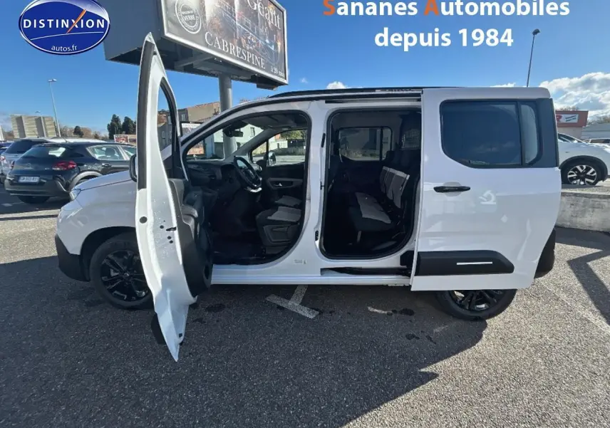 Vue latérale gauche d’un Citroën Berlingo blanc avec portes avant et latérale ouvertes, jantes noires et sièges arrière visibles.
