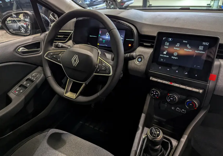 Vue intérieure côté conducteur de la Renault Clio V gris Rafale, avec volant multifonction et écran tactile central allumé.
