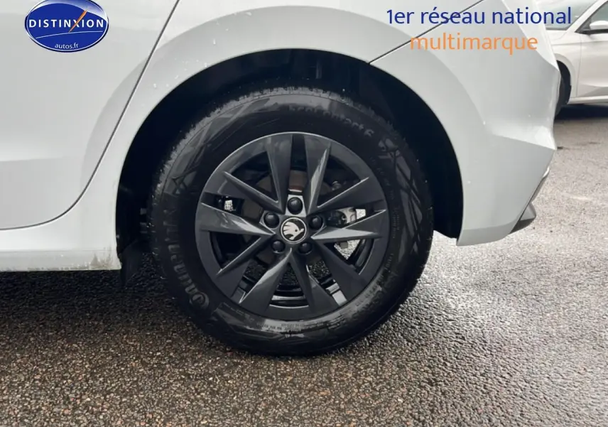Gros plan sur la roue arrière gauche avec jante alu noire d'une Skoda Fabia blanche, vue de profil partiel.
