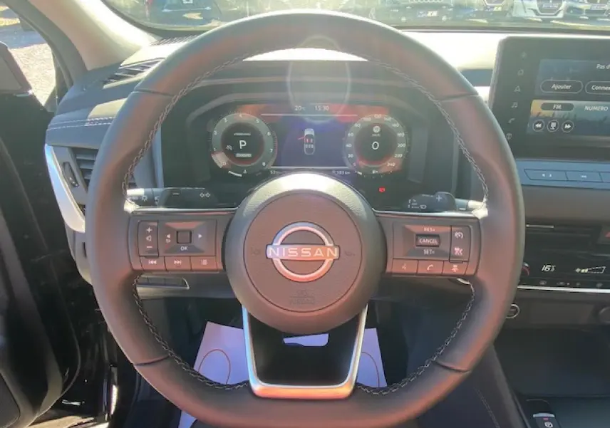 Vue intérieure centrée sur le volant noir du Nissan Qashqai 2023 avec tableau de bord numérique et commandes intégrées.